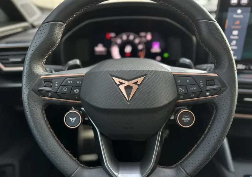 Gros plan sur le volant cuir perforé noir avec logo CUPRA cuivré et commandes multifonctions du Formentor Blanc Neige 2025.
