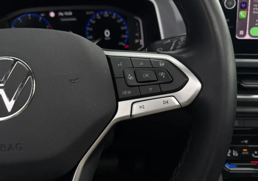 Gros plan sur le volant multifonction noir avec commandes intégrées du Volkswagen T-Roc 2024, tableau de bord numérique en arrière-plan.