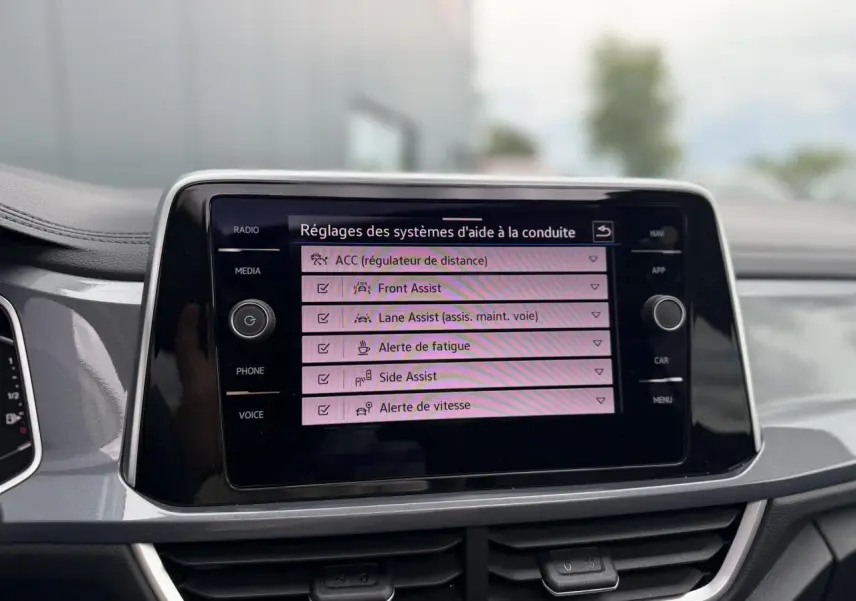 Écran tactile central du Volkswagen T-Roc 2024 affichant les réglages des aides à la conduite, tableau de bord gris argent.