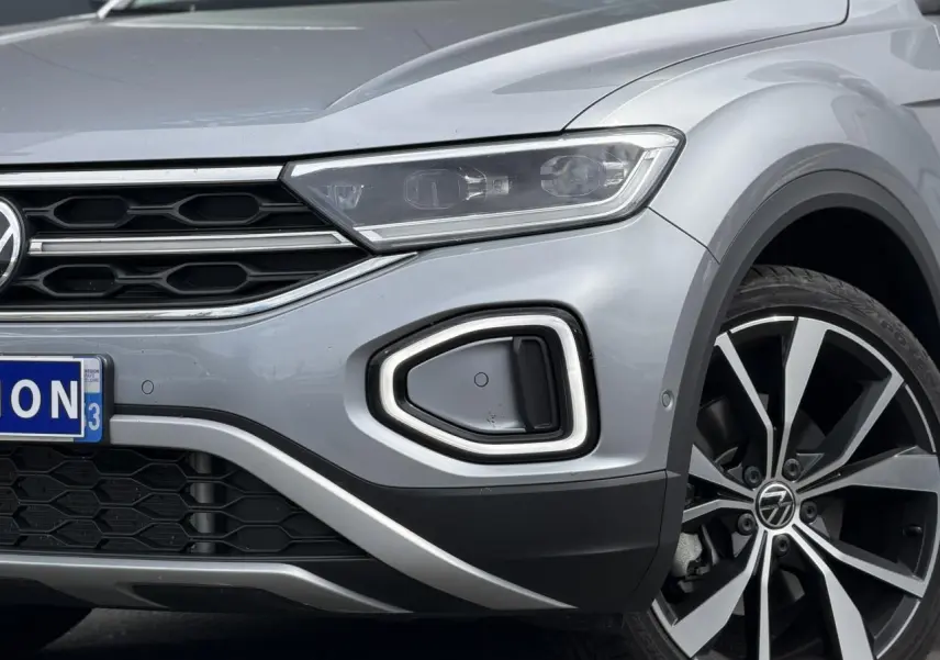 Gros plan sur l'avant droit du Volkswagen T-Roc argent Pyrite, mettant en valeur le phare LED et la jante alliage 19 pouces.