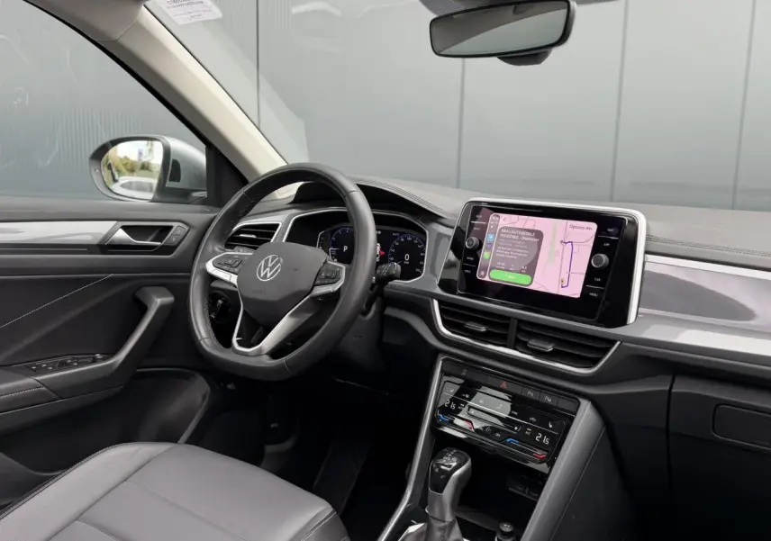 Vue intérieure côté conducteur du Volkswagen T-Roc 2024 avec tableau de bord noir et écran tactile central allumé.