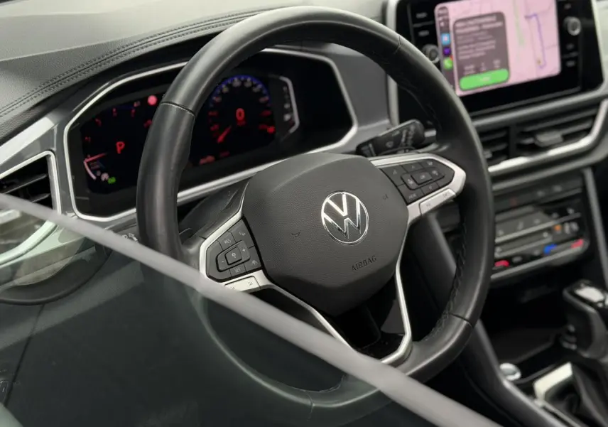 Vue intérieure centrée sur le volant en cuir noir du Volkswagen T-Roc 2024 avec tableau de bord numérique et écran tactile.