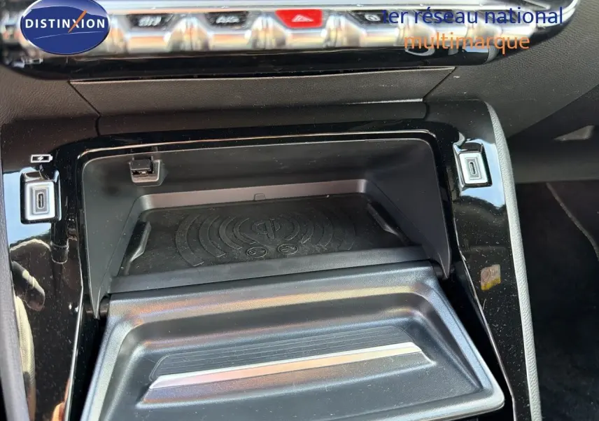 Gros plan sur la console centrale du Peugeot 2008 1.2 HYBRID 145 GT, montrant un compartiment de rangement avec chargeur sans fil.