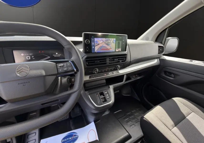 Vue intérieure côté conducteur du tableau de bord gris avec écran tactile et volant multifonctions du Citroën Jumpy gris foncé.