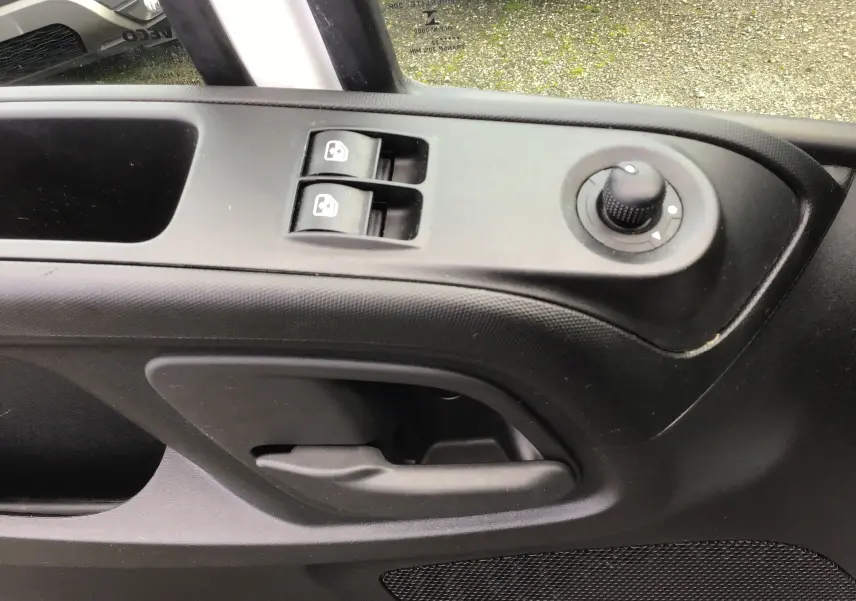 Gros plan sur la commande des vitres électriques et le réglage des rétroviseurs côté conducteur d'un Iveco Daily blanc.