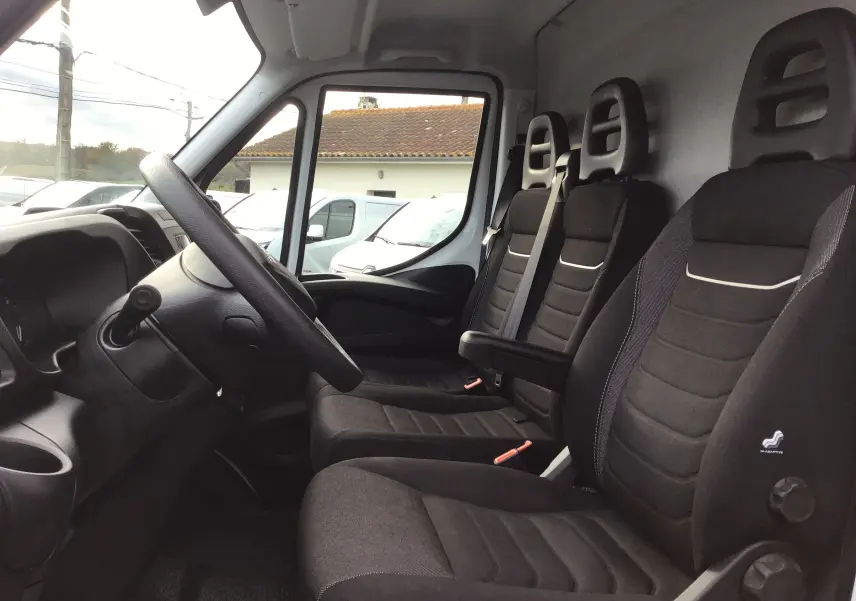 Vue intérieure côté conducteur de l'Iveco Daily Fourgon 2022 avec sièges noirs et tableau de bord gris.