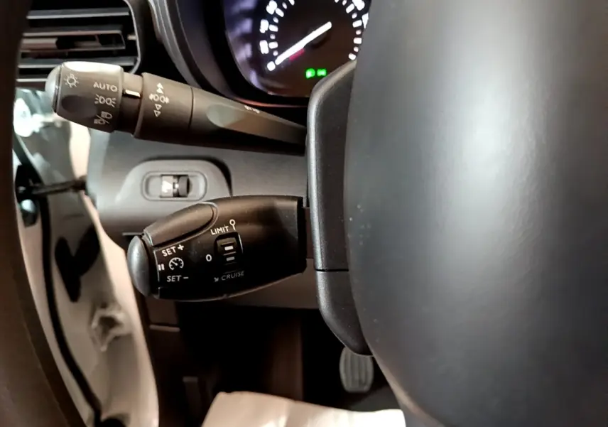 Gros plan sur la commande de régulateur de vitesse à gauche du volant du Citroën Berlingo blanc, tableau de bord en arrière-plan.