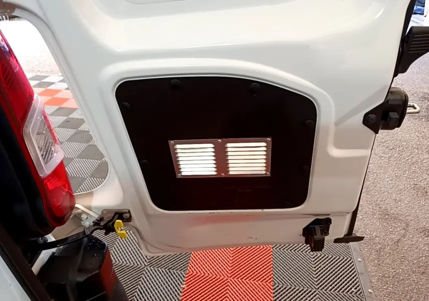 Détail de la porte arrière gauche ouverte d'un Citroën Berlingo blanc, montrant une cloison pleine avec grille d'aération.