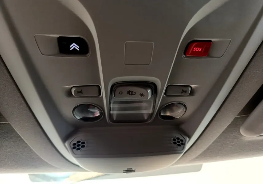 Vue en contre-plongée du plafonnier gris clair du Citroën Berlingo 2021 avec boutons d'éclairage et alarme SOS rouge.