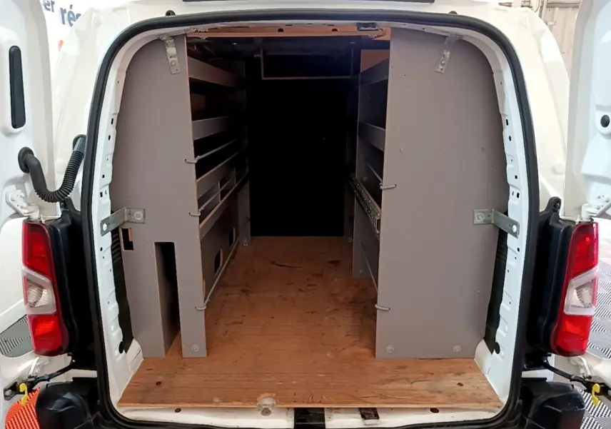 Vue arrière du Citroën Berlingo blanc 2021 avec portes ouvertes dévoilant un aménagement intérieur en bois et étagères grises.