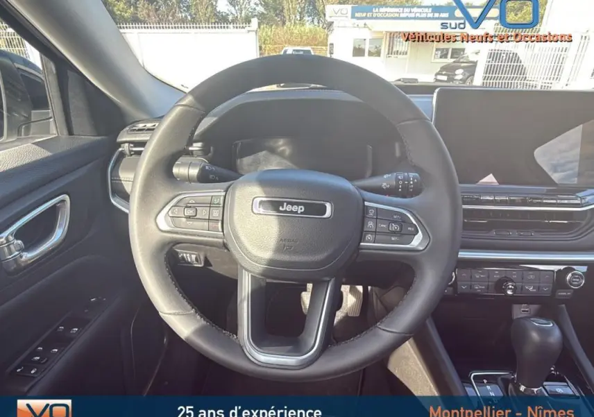 Vue intérieure centrée sur le volant du Jeep Compass blanc 2024 avec tableau de bord et écran tactile visibles.