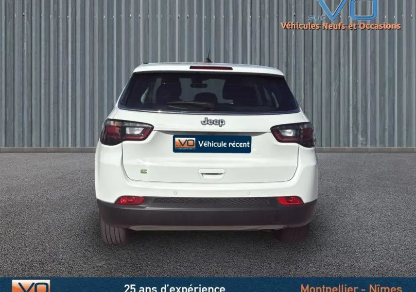 Vue arrière d'un Jeep Compass blanc 2024 avec feux LED et logo Jeep visible sur un fond industriel.