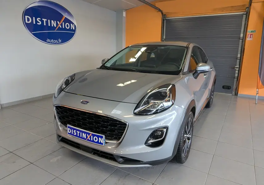 Ford Puma gris en 3/4 avant droit, avec calandre noire et phares LED, stationné en intérieur showroom.