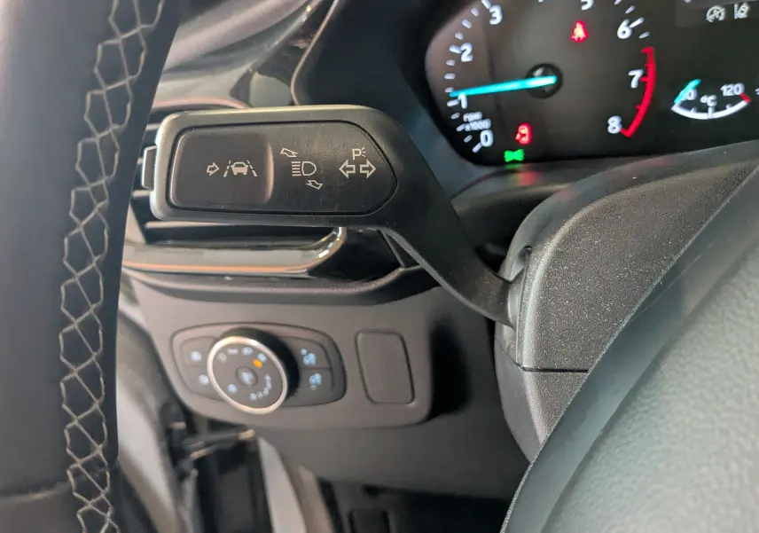Détail de la commande des feux et clignotants côté gauche du volant d’un Ford Puma gris, tableau de bord en arrière-plan.