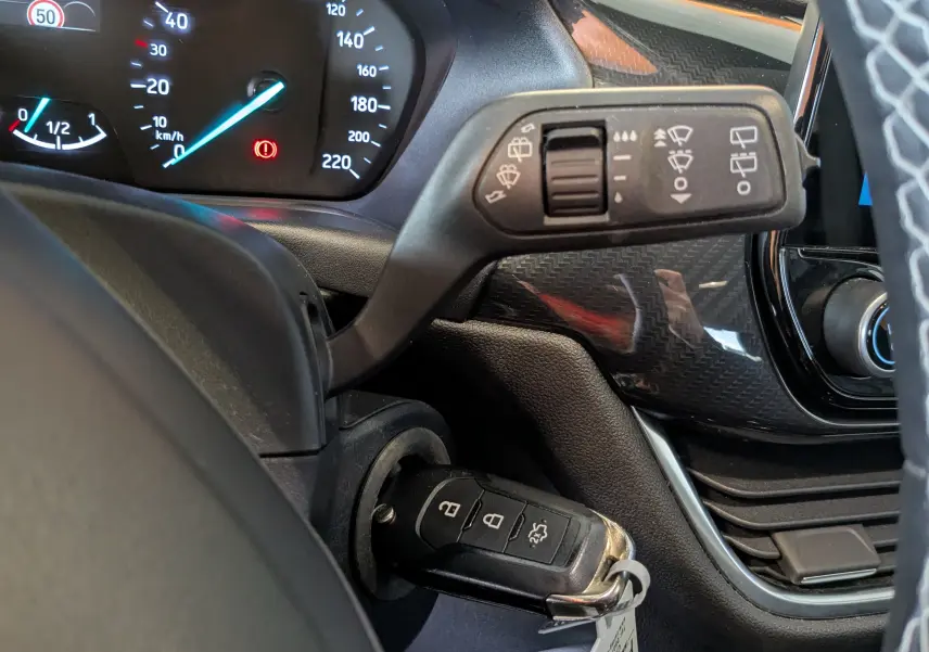 Gros plan sur la colonne de direction et le tableau de bord du Ford Puma gris, avec clé insérée et commandes d’essuie-glace visibles.