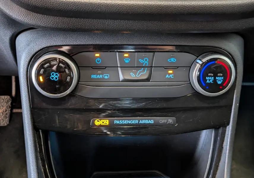 Gros plan sur la console de climatisation du Ford Puma gris 2020, avec commandes rotatives et voyants lumineux allumés.