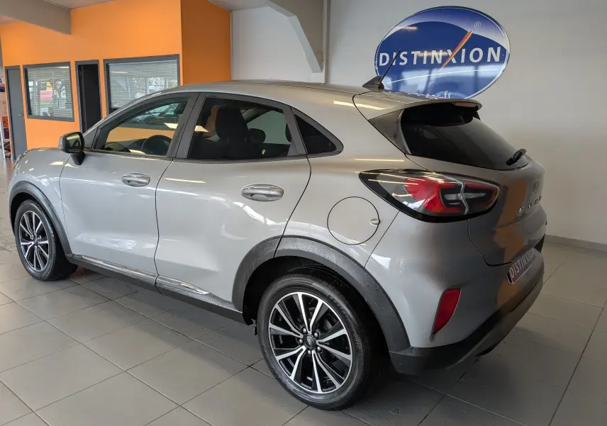 Vue 3/4 arrière droite d’un Ford Puma gris métallisé 2020 avec jantes alliage bicolores et vitres teintées, en intérieur showroom.