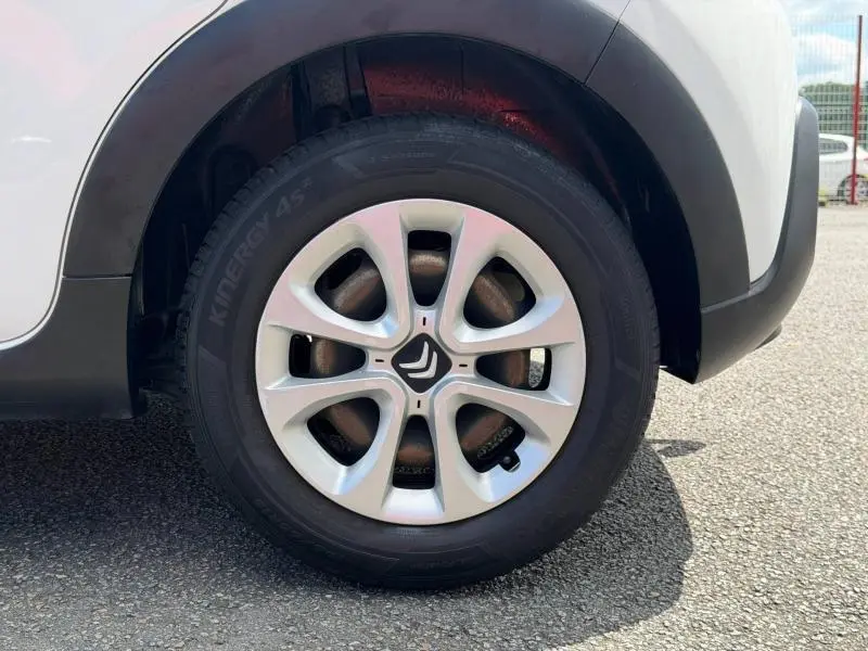 Gros plan sur la roue avant droite d'une Citroën C3 blanc banquise avec jante argentée et entourage noir.