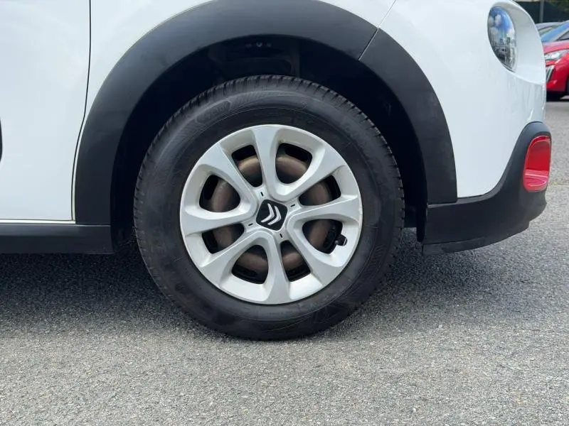 Gros plan sur la roue avant droite d'une Citroën C3 blanche avec jante argentée et détails rouges sur le pare-chocs.