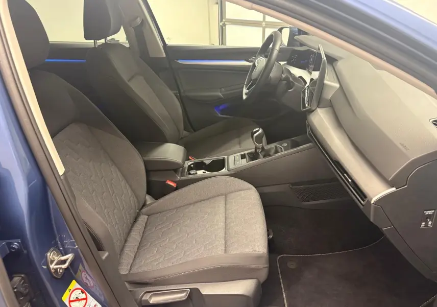 Vue intérieure côté conducteur de la Volkswagen Golf 1.5 TSI Bleu Anémone avec sièges tissu gris et éclairage d'ambiance bleu.
