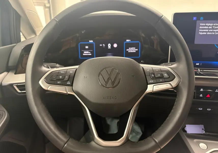 Vue rapprochée du volant noir de la Volkswagen Golf 1.5 TSI 2025 avec commandes intégrées et tableau de bord numérique.