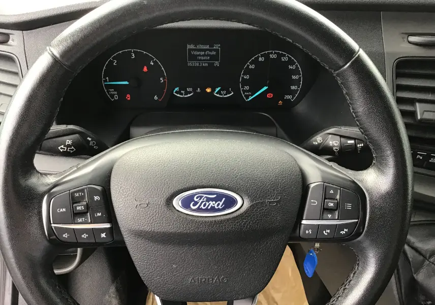 Vue rapprochée du volant en cuir noir et du tableau de bord du Ford Transit Fourgon blanc de 2020.