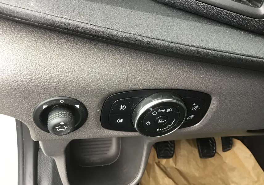 Gros plan sur les commandes d'éclairage et de réglage du tableau de bord du Ford Transit Fourgon blanc, côté conducteur.
