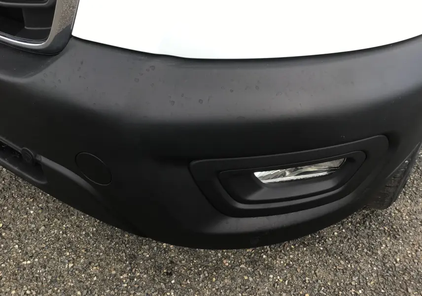 Gros plan sur le pare-chocs avant droit noir et antibrouillard du fourgon Ford Transit blanc de 2020.