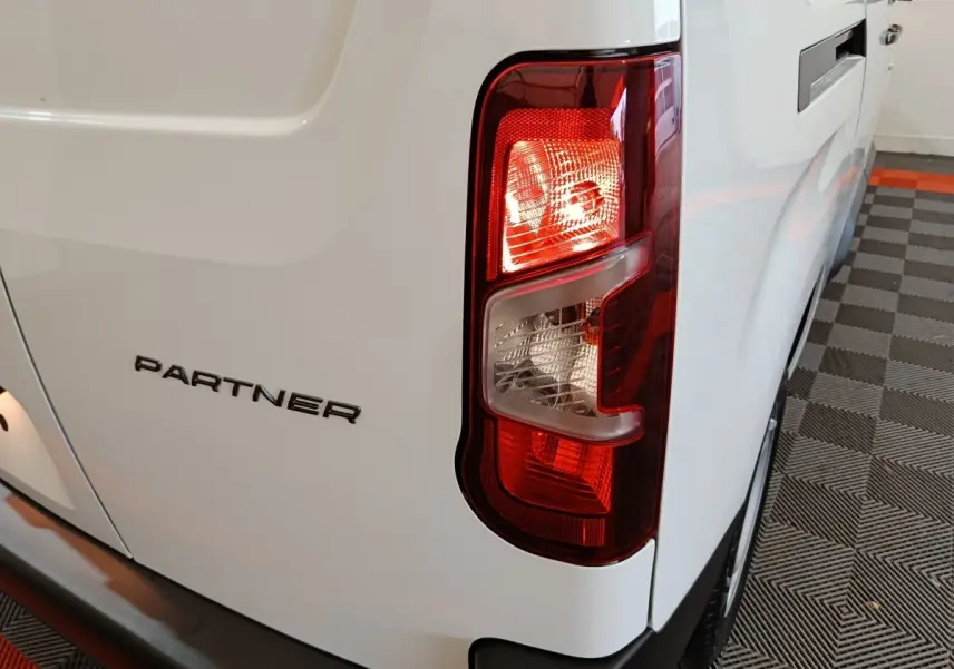 Gros plan sur le feu arrière droit d’un Peugeot Partner blanc XL 950kg, avec logo visible sur la porte arrière.