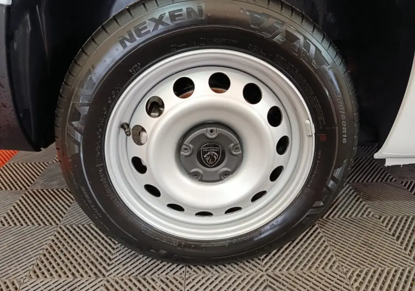 Gros plan sur la roue avant droite du Peugeot Partner blanc 2025 avec jante acier et logo Peugeot au centre.