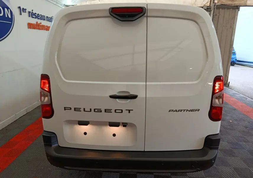 Vue arrière du Peugeot Partner blanc 2025 avec portes battantes et feux arrière allumés dans un garage.