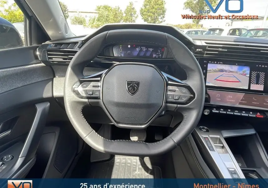 Vue intérieure centrée sur le volant noir de la Peugeot 308 gris, avec tableau de bord numérique et écran tactile affichant la caméra de recul.