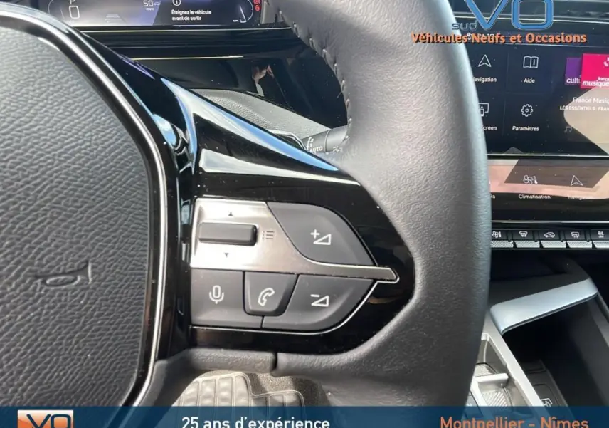 Gros plan sur les commandes au volant gauche d'une Peugeot 308 gris, avec affichage numérique et écran tactile visible.