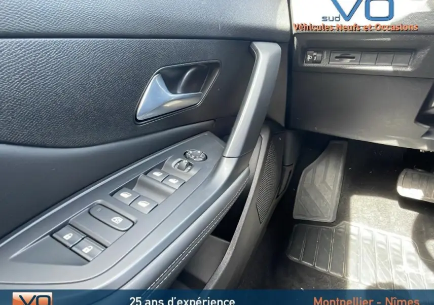 Vue rapprochée de la porte côté conducteur d’une Peugeot 308 gris, montrant les commandes des vitres électriques et la poignée intérieure.