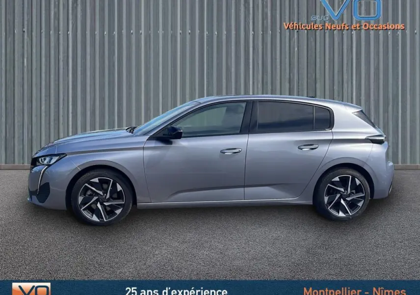 Vue latérale droite d'une Peugeot 308 gris métallisé 2024, avec jantes alliage et vitres teintées, sur fond industriel.