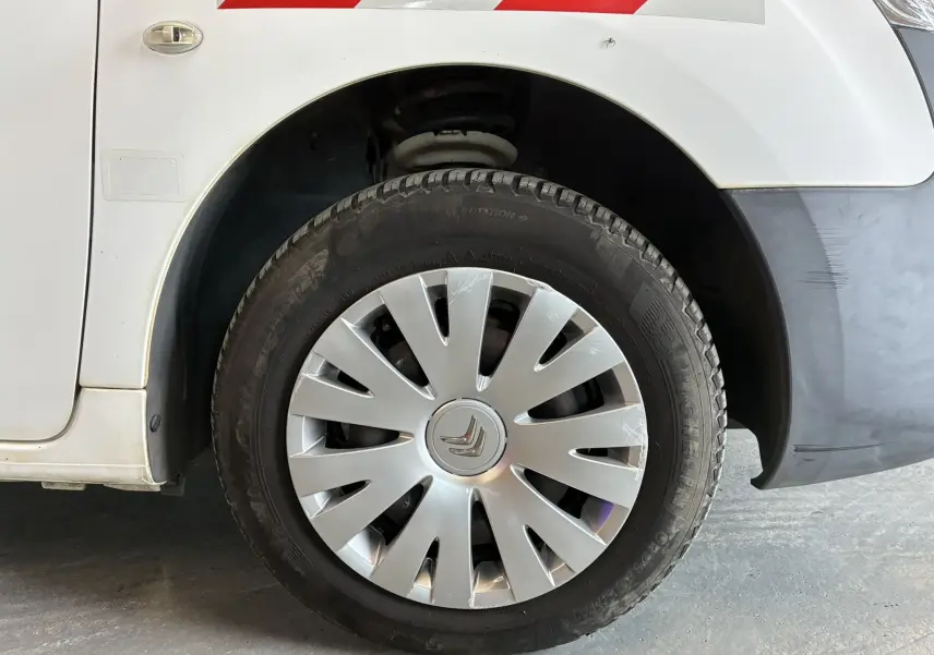 Gros plan sur la roue avant gauche d’un Citroën Berlingo blanc de 2016 avec enjoliveur argenté et pare-chocs noir.