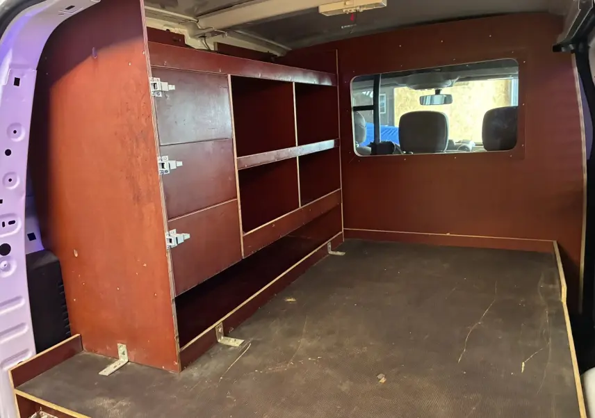 Vue intérieure arrière droite du Citroën Berlingo blanc 2016, montrant un aménagement bois avec étagères et fenêtre vers l'avant.