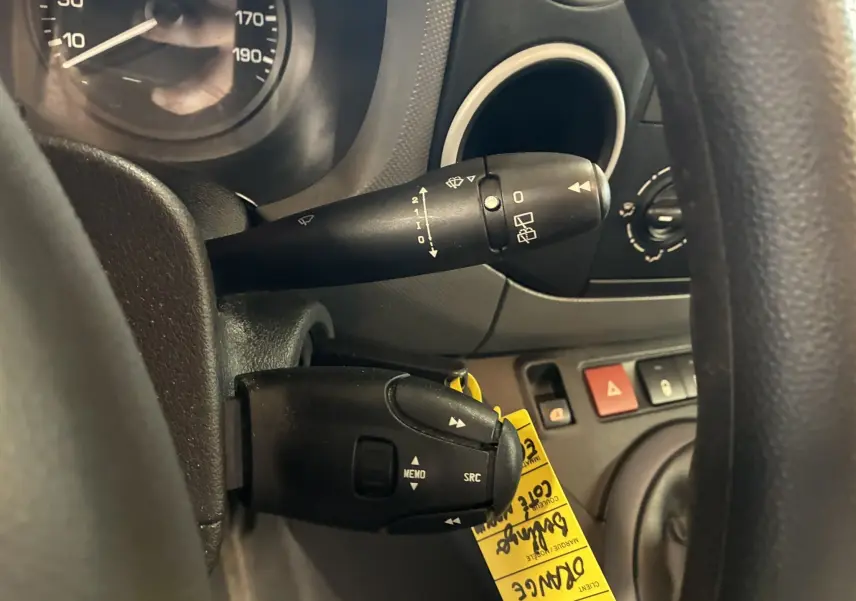 Gros plan sur les commandes au volant et levier d’essuie-glace du tableau de bord noir du Citroën Berlingo blanc 2016.