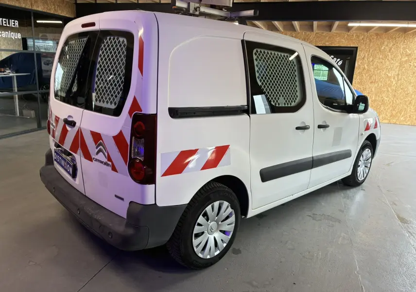 Vue 3/4 arrière droit d'un Citroën Berlingo blanc 2016 avec marquages rouges réfléchissants et grilles de protection aux vitres.