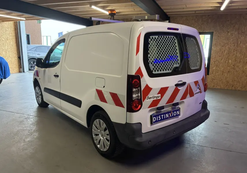 Vue 3/4 arrière droite d’un Citroën Berlingo blanc utilitaire avec bandes réfléchissantes rouges et grilles sur les vitres arrière.