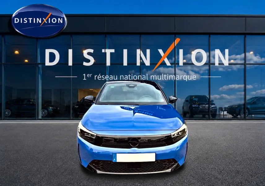 Vue frontale d'une Opel Corsa 1.2 turbo 100 gs bleu avec calandre noire et phares LED devant un showroom Distinxion.