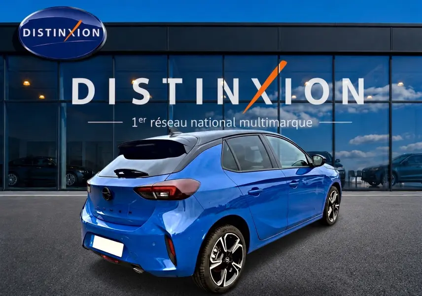 Vue 3/4 arrière droite d'une Opel Corsa bleu 2025 avec toit noir et jantes alu distinctives, devant une vitrine Distinxion.