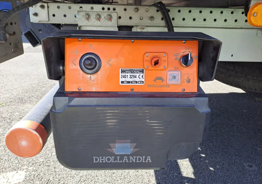 Gros plan sur la commande orange et noire Dhollandia sous le châssis d’un Nissan Interstar blanc, côté arrière droit.