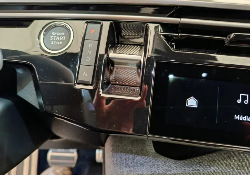 Gros plan sur la console centrale noire brillante du Peugeot 3008 hybride 2025 avec bouton start et commandes de boîte auto.