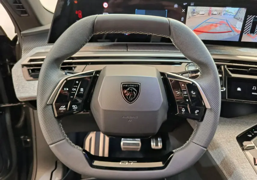 Vue rapprochée du volant cuir gris perforé avec logo Peugeot et badge GT du Peugeot 3008 hybride 2025.