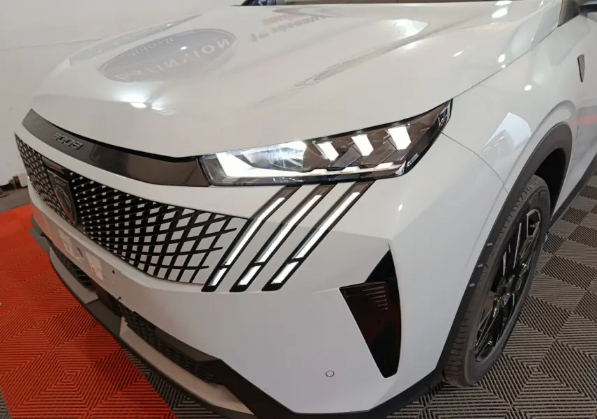Vue 3/4 avant droit du Peugeot 3008 blanc avec calandre à motif losange et phares LED distinctifs en griffes.