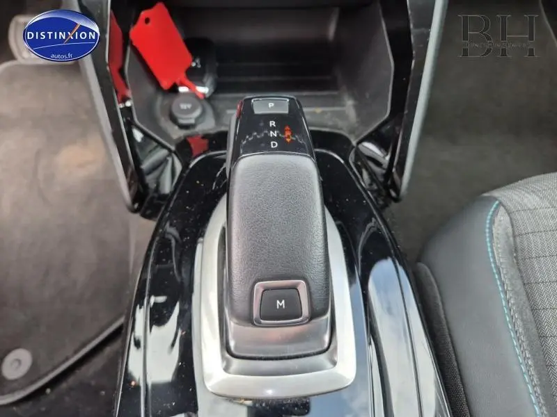 Gros plan sur le levier de vitesses automatique noir brillant de la Peugeot 2008, avec bouton M visible, intérieur tissu gris.
