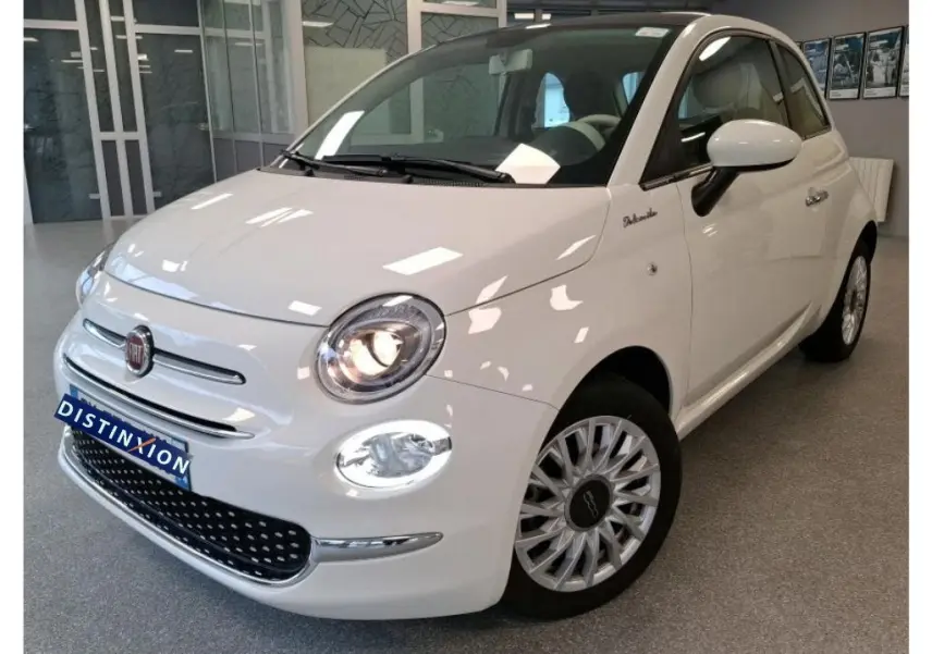 Vue 3/4 avant d'une Fiat 500 blanche Bossa Nova, avec phares allumés et jantes distinctives en concession.