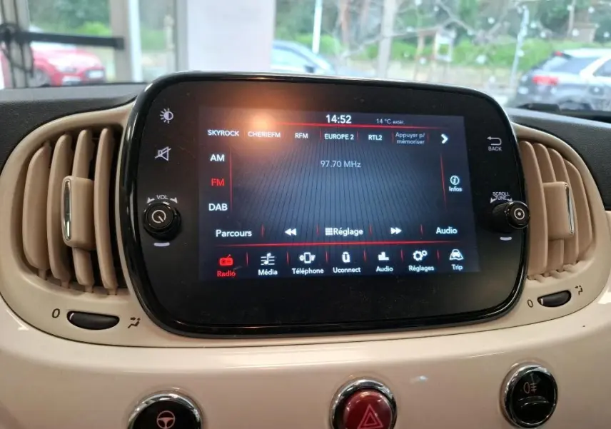 Écran tactile central du tableau de bord beige de la FIAT 500 blanche, affichant la radio FM à 97,70 MHz.