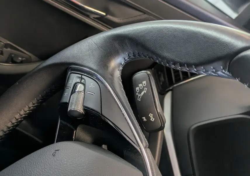 Gros plan sur le volant cuir noir côté gauche du Skoda Karoq 2023, avec commandes intégrées et rétroviseur extérieur visible.